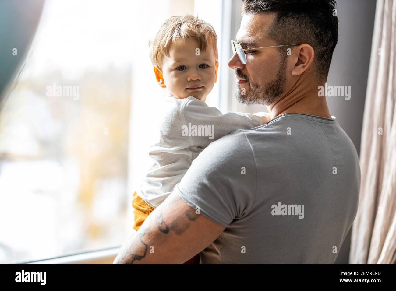 Mann mit seinem kleinen Sohn, der durch das Fenster schaut Zu Hause Stockfoto
