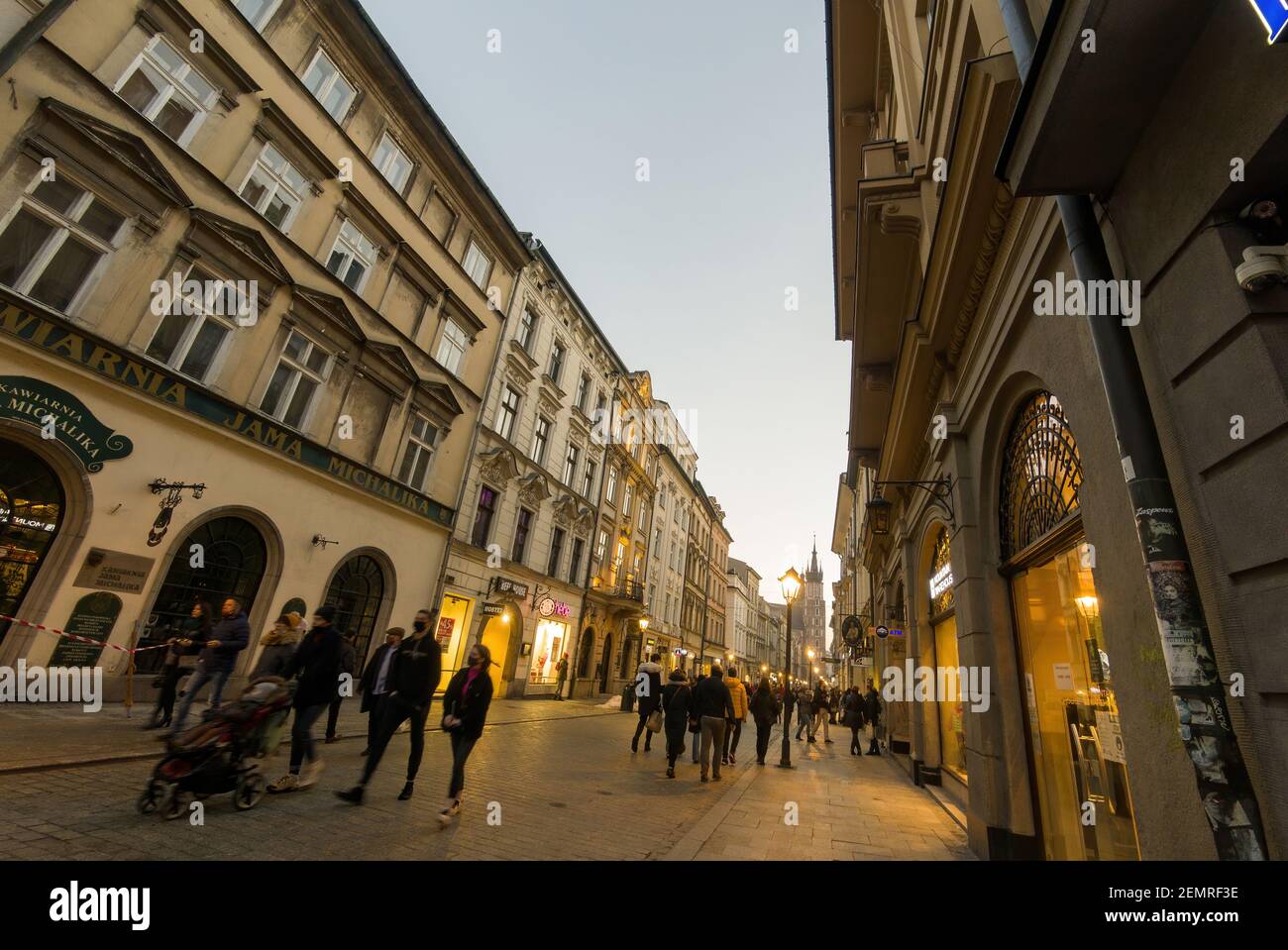 Krakau, Polen - 20. Februar 2021: Weitwinkelaufnahme einer europäischen Straße und Menschen, die abends in der Altstadt von krakau spazieren gehen. Peopl Stockfoto