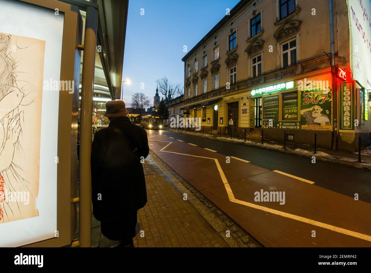 Krakau, Polen - 20. Februar 2021: Hinter einer Frau in Winterkleidung und Mütze, die in einem Busstand steht und auf eine Busankunft gegen polnische Kommerci wartet Stockfoto