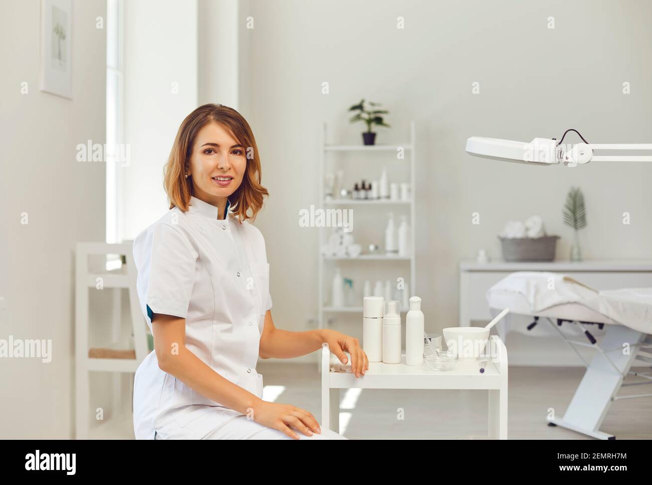 Kosmetologe oder Dermatologe Blick auf Kamera im Schönheitssalon mit Verschiedene Kosmetika im Hintergrund Stockfoto
