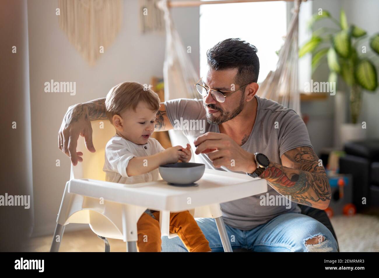 Single Papa Fütterung sein Baby, das in einem gesessen wird Kinderstuhl Stockfoto