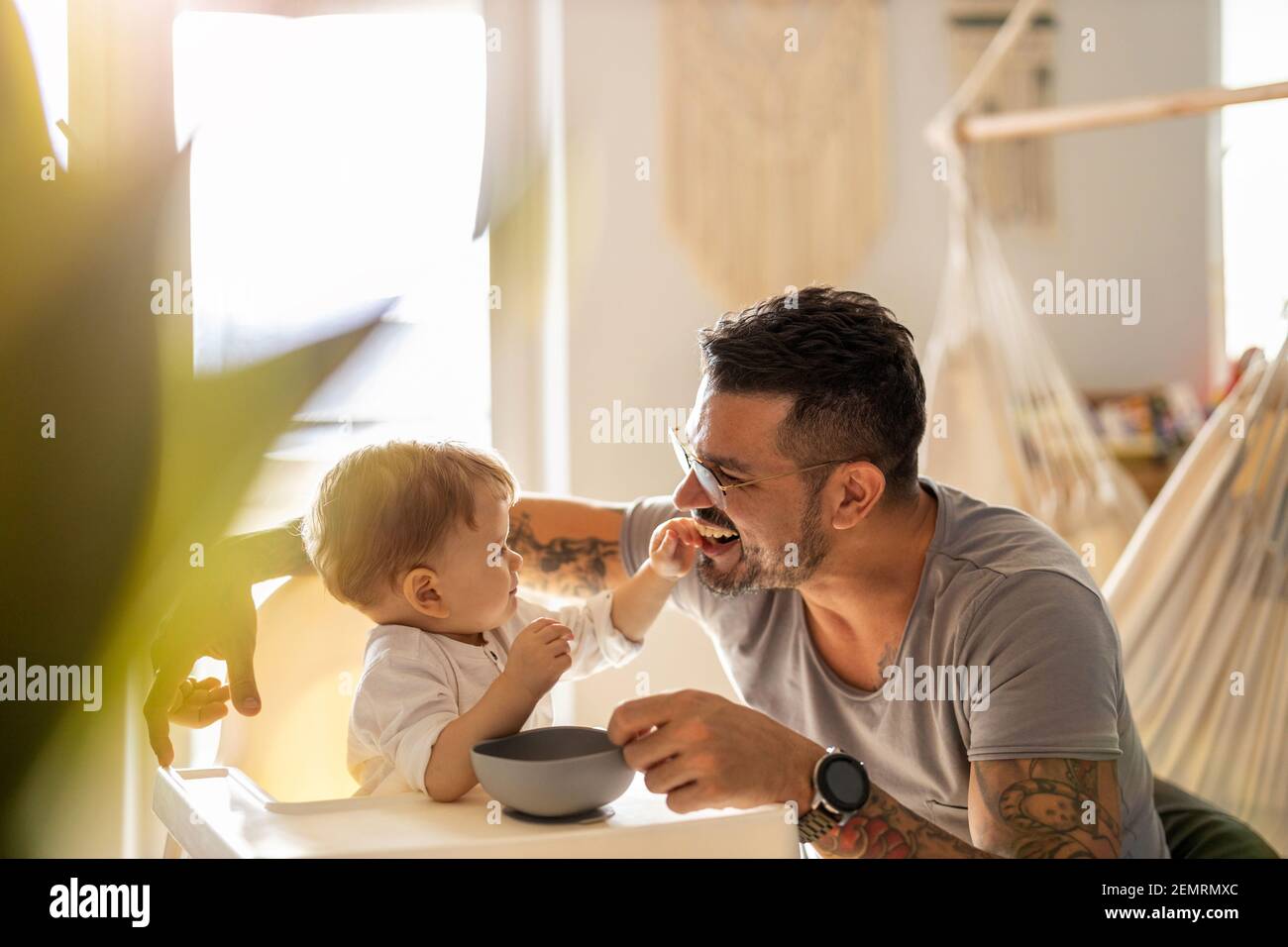 Single Papa Fütterung sein Baby, das in einem gesessen wird Kinderstuhl Stockfoto