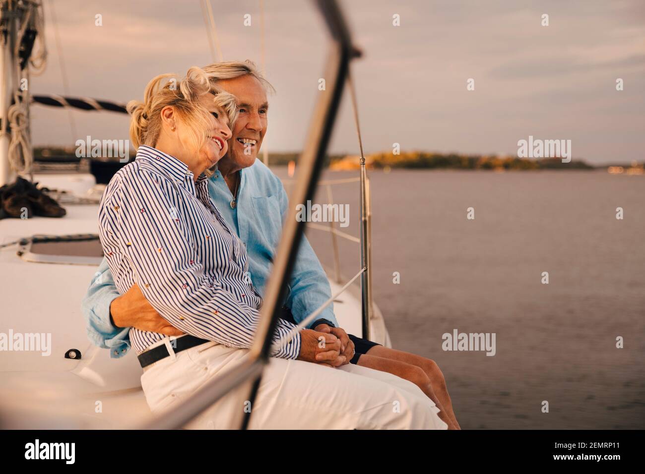 Glückliches Seniorenpaar, das während des Sonnenuntergangs am Rand des Segelbootes sitzt Stockfoto