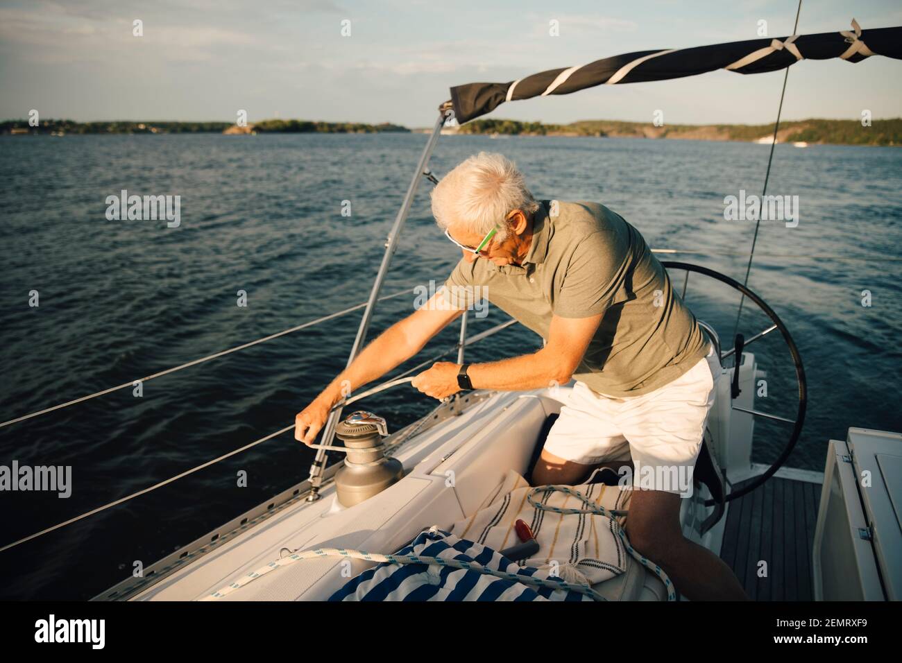Älterer Mann, der beim Knien im Boot Seil an Strang bindet An sonnigen Tagen Stockfoto