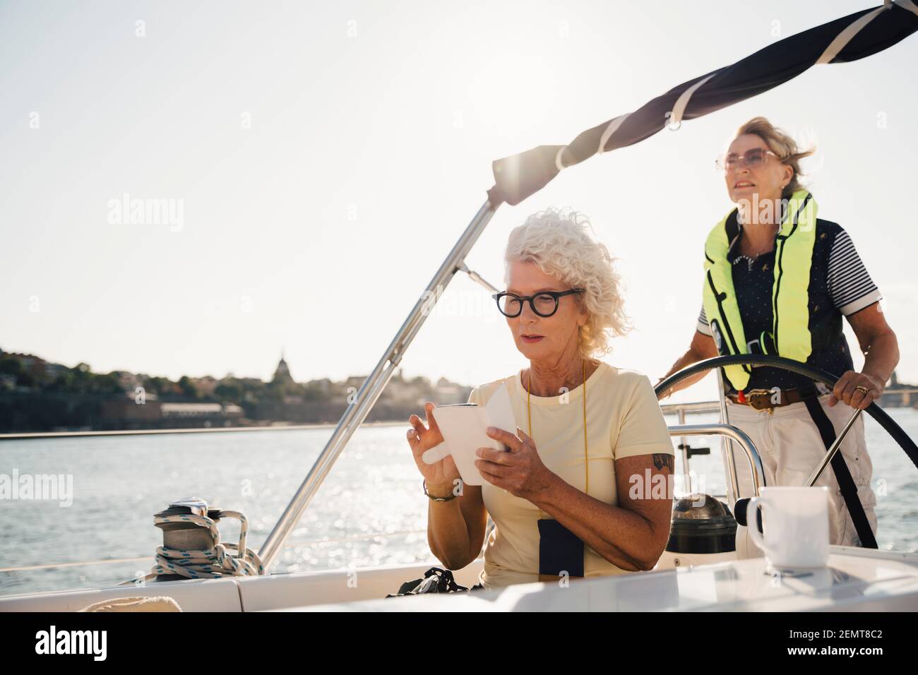 Ältere Frau, die auf dem Smartphone navigiert, während sie ein Segelboot segelt Gegen den Himmel Stockfoto