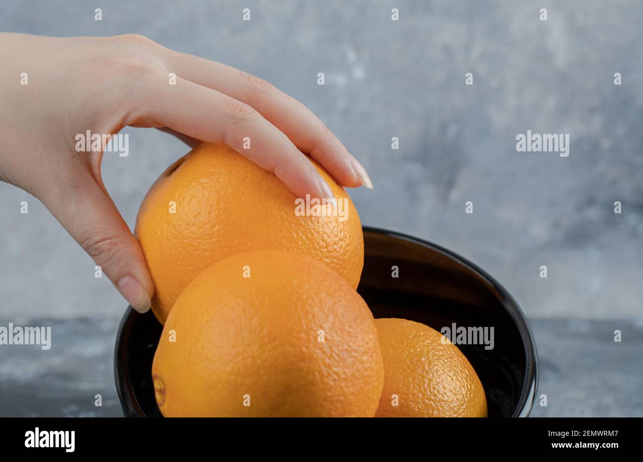 Weibliche Hand, die frische Orange aus der schwarzen Schale nimmt Stockfoto