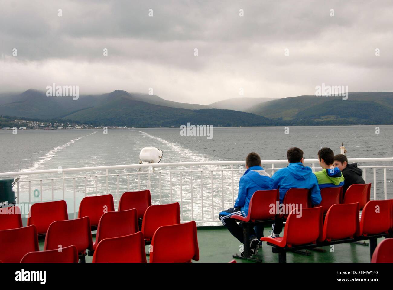 Vier junge Männer, die am Heck einer Fähre sitzen und die Wake betrachten, während sie den Firth of Clyde, Schottland, überqueren Stockfoto