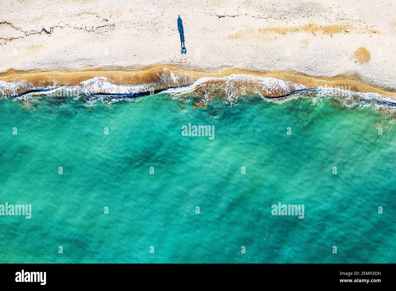 Luftaufnahme einer einzigen menschlichen Figur, die Schatten auf Sandstrand wirft, am Meer mit wunderschönem azurblauen tropischen Meerwasser und Wellen steht, kopieren Sie Platz für Ihren Text. Stockfoto