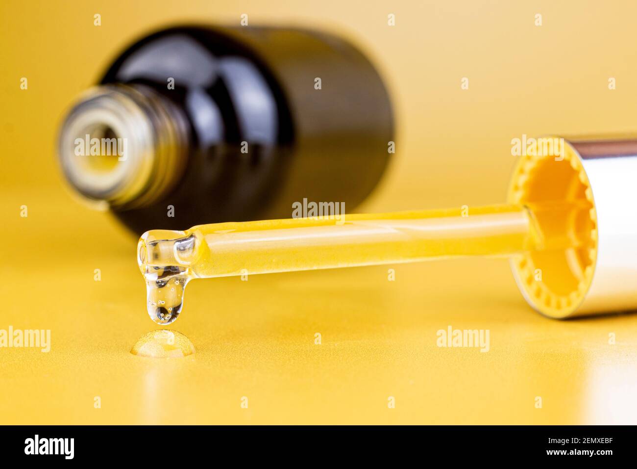 Kosmetische Pipette und Flasche mit einem Tropfen kosmetischen Öl oder Serum auf gelbem Hintergrund. Nahaufnahme des Bildes. Stockfoto