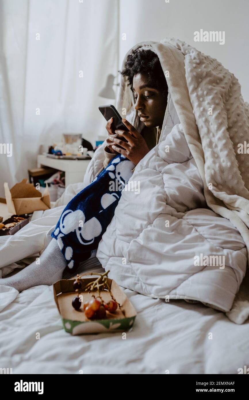 Junge Frau SMS-Nachrichten über Smartphone, während sitzen auf Bett zu Hause Stockfoto