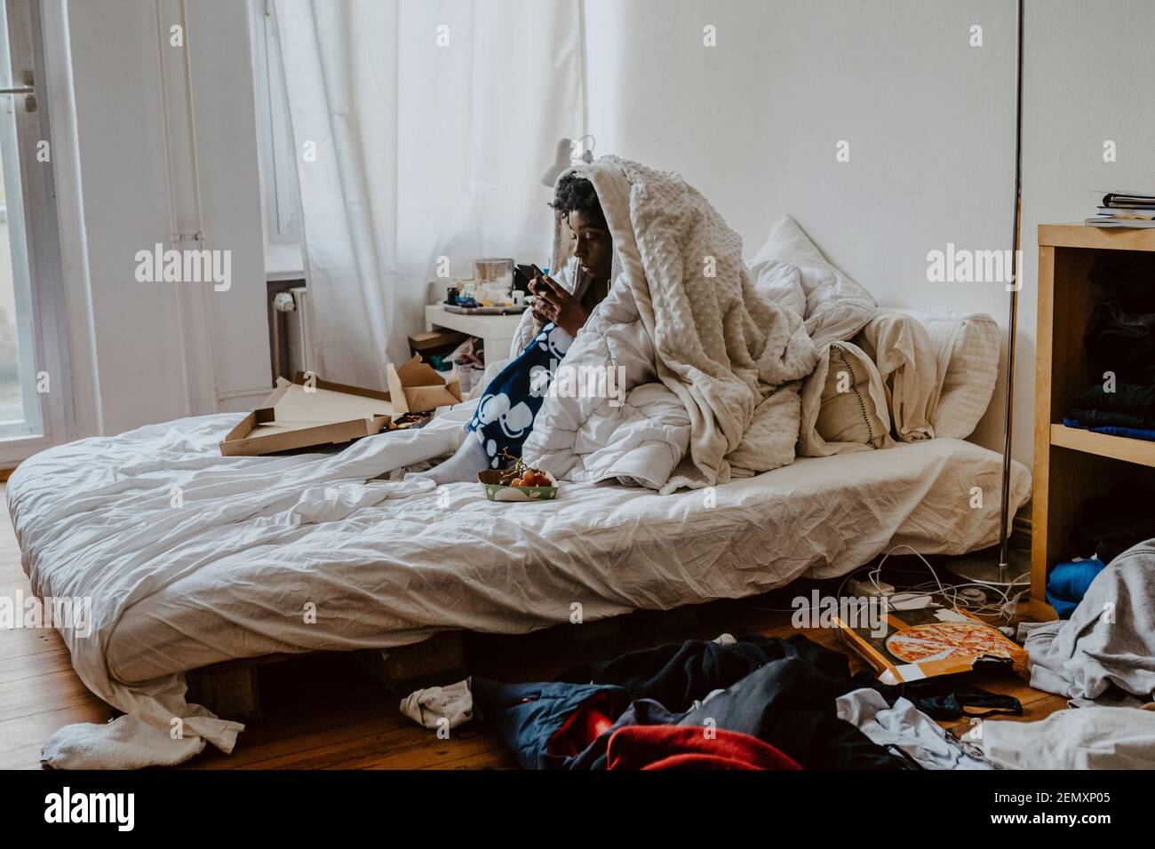 Frau SMS auf Smartphone, während sie im Schlafzimmer sitzt Stockfoto
