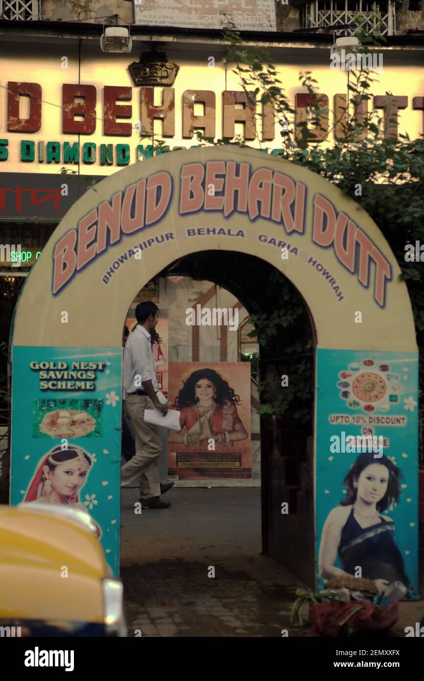 Ein Mann, der auf dem Gehweg eines Geschäftsviertels läuft, gesehen durch ein Tor am Straßenrand mit Werbung in Kalkutta, Westbengalen, Indien. Stockfoto