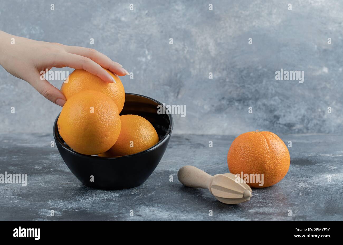 Weibliche Hand, die frische Orange aus der schwarzen Schale nimmt Stockfoto