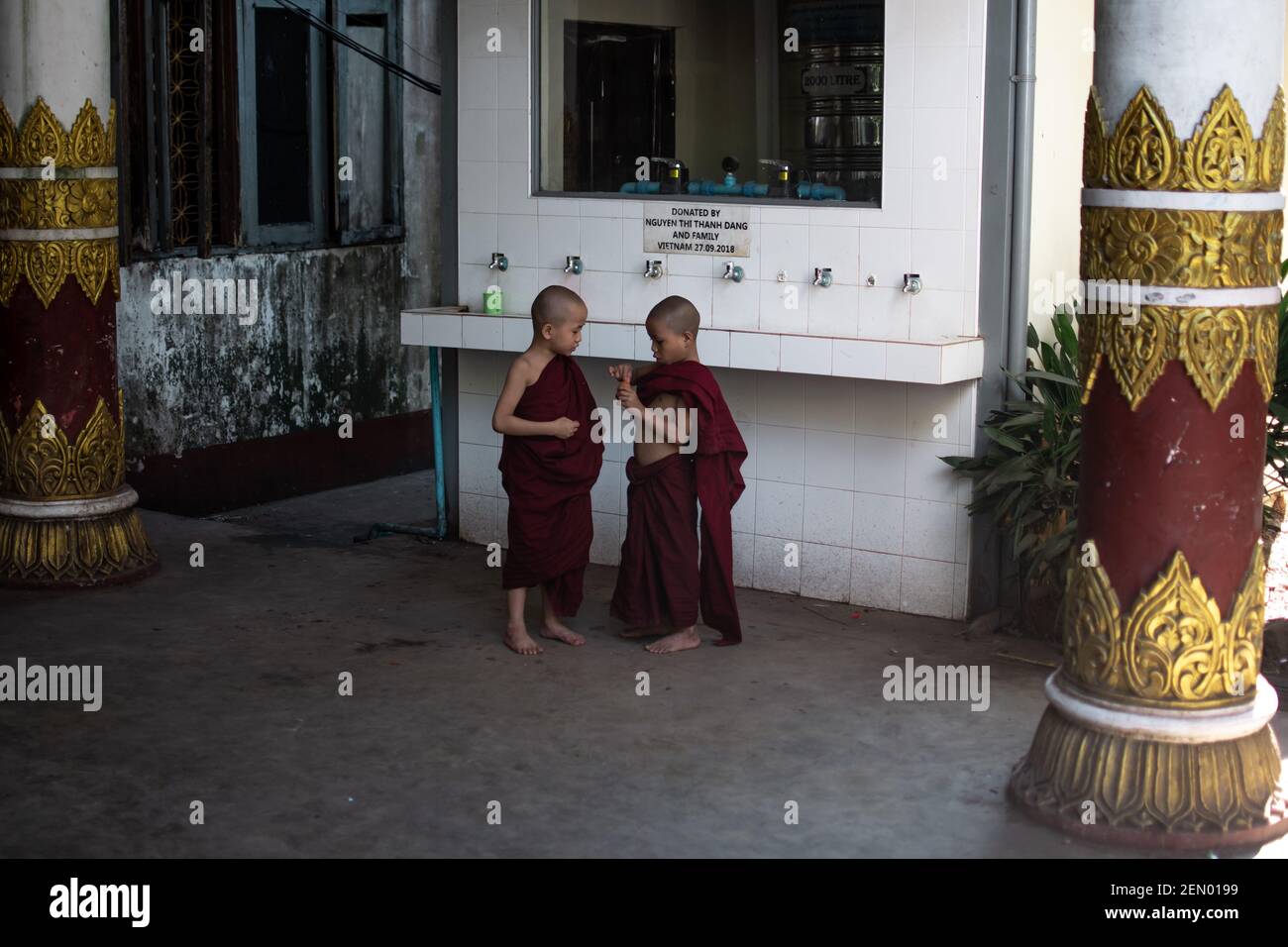 YANGON, MYANMAR - JANUAR 1 2020: Zwei junge Mönche in traditionellen roten Roben stehen zusammen an der SWE Taw Myat Pagode Stockfoto