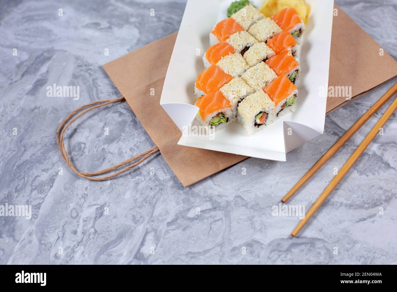Takeaway-Box mit Sushi-Rollen auf braunem Papierbeutel. Sushi-to-go-Konzept. Stockfoto