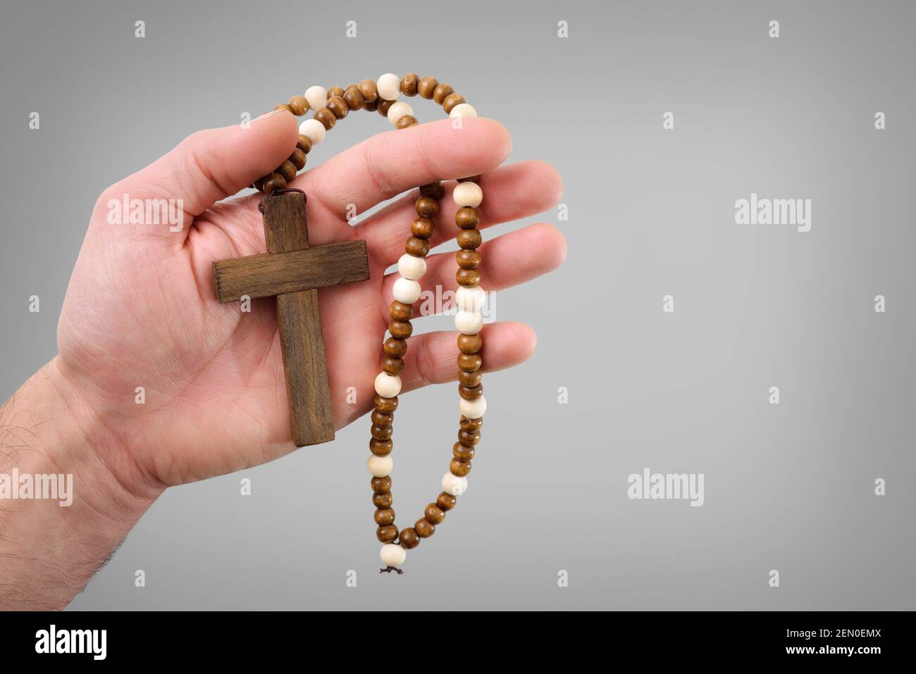 Christliches Holzkreuz mit runden Holzperlen auf der Hand Eines religiösen Anhängers mit isoliertem grauen Hintergrund Stockfoto