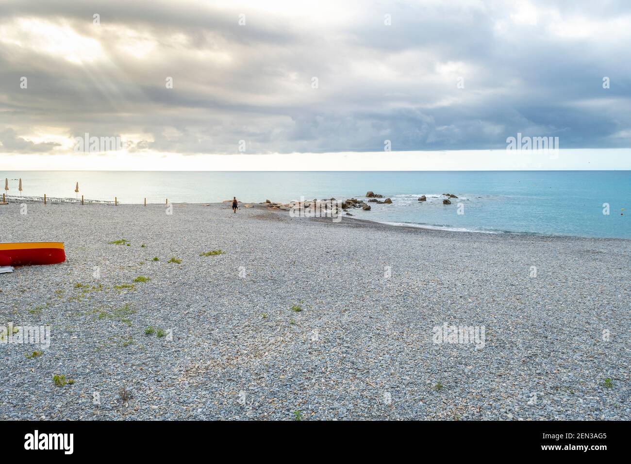 Ein einsamer Mann geht entlang der Küste und Strand in Ventimiglia, Italien, während die Sonne an der italienischen Riviera aufgeht. Stockfoto