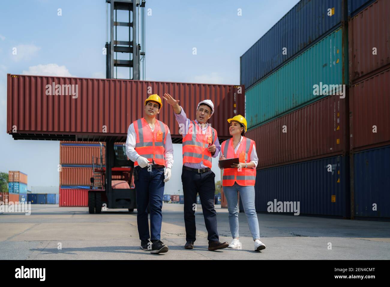 Asiatischer Vorarbeiter geht und erklärt den Arbeitern die verschiedenen Operationen im Containerdepot-Terminal. Stockfoto
