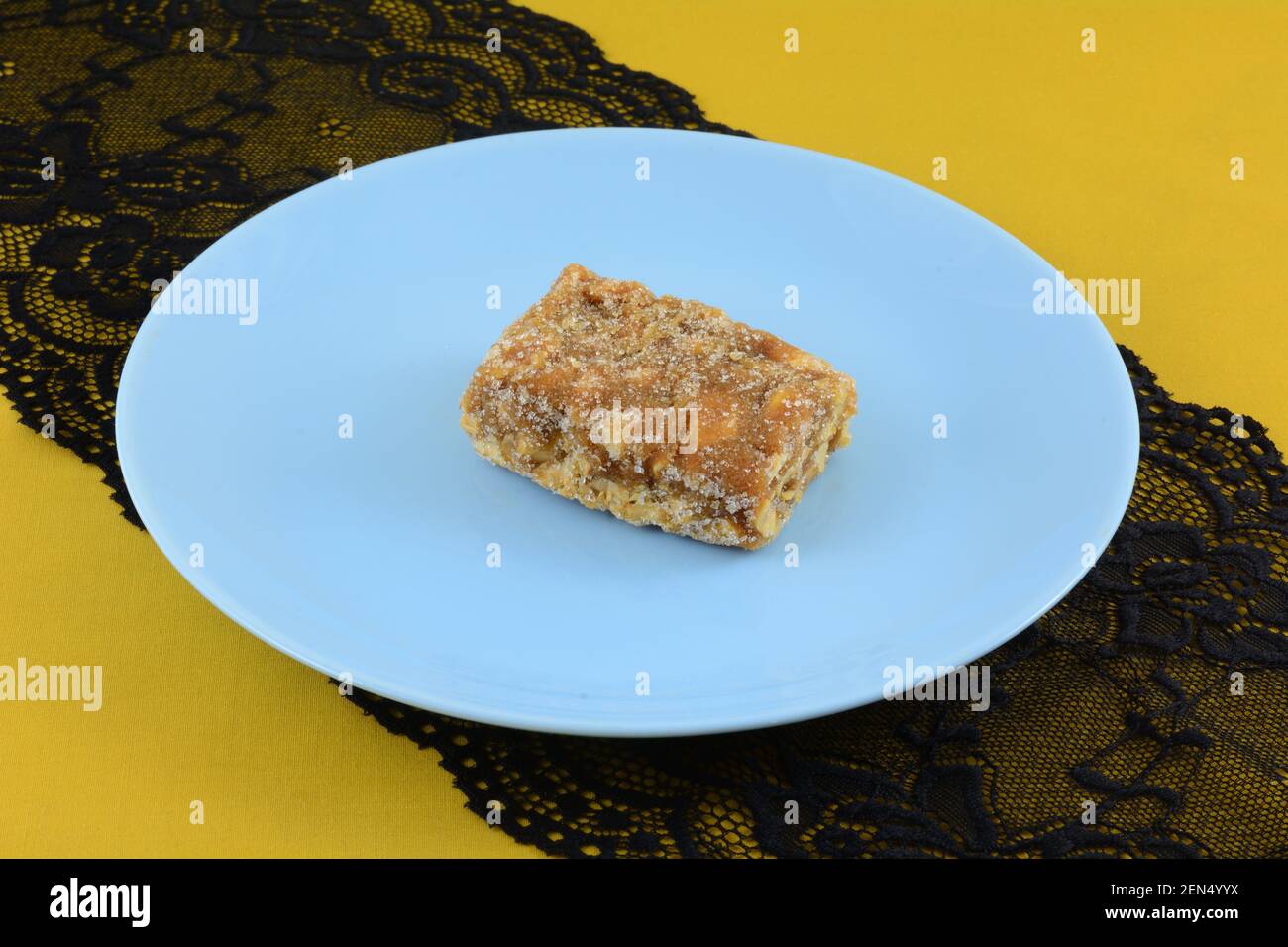 Brasilianisches pe de moca oder Erdnussspröde Toffee auf Blau Snackplatte auf schwarzem Spitzentischläufer auf gelbem Ocker Tischdecke Stockfoto