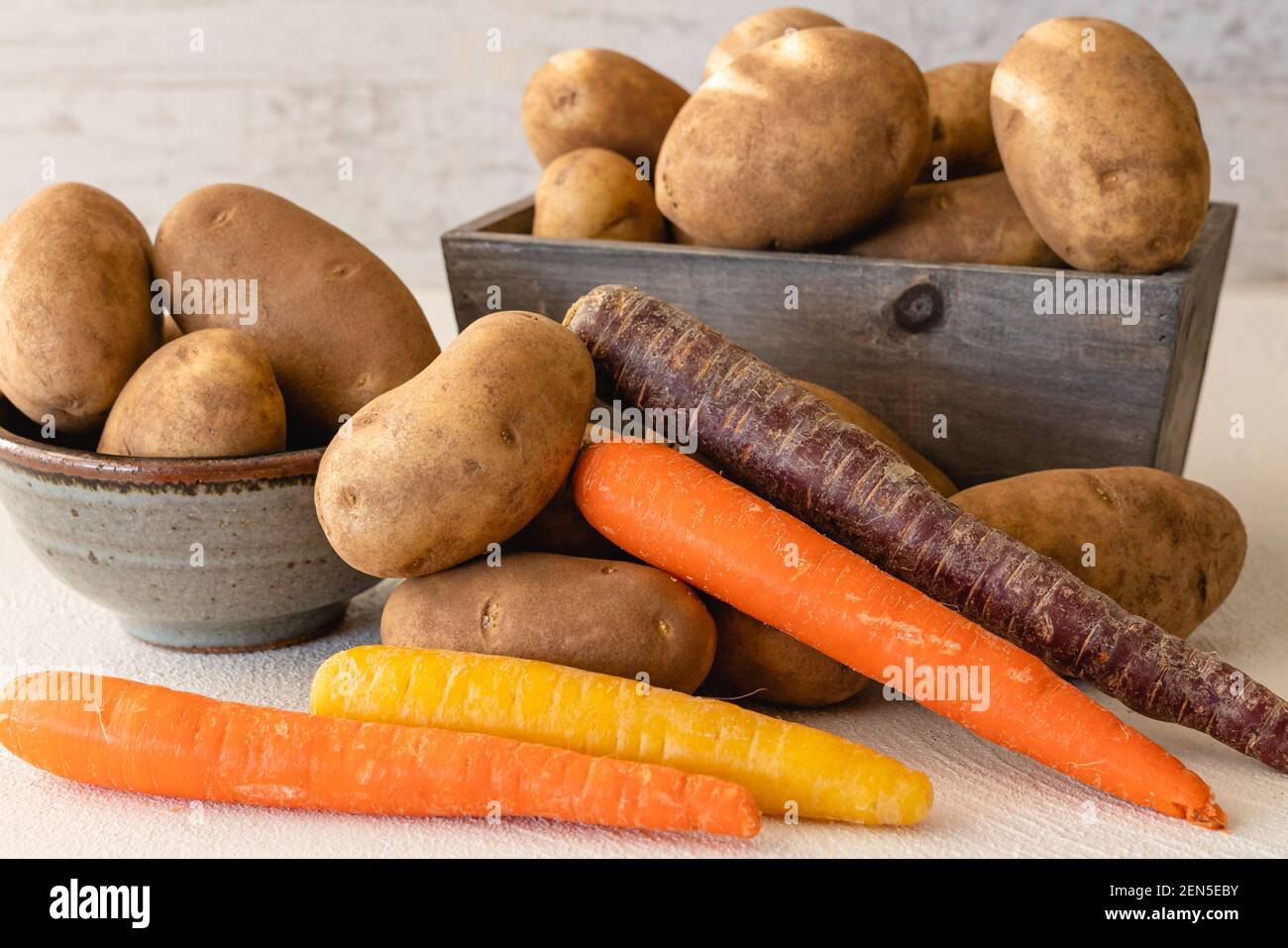 Bio-Karotte in vielen Farben und Kartoffeln aus nächster Nähe Weißer Küchentisch Stockfoto