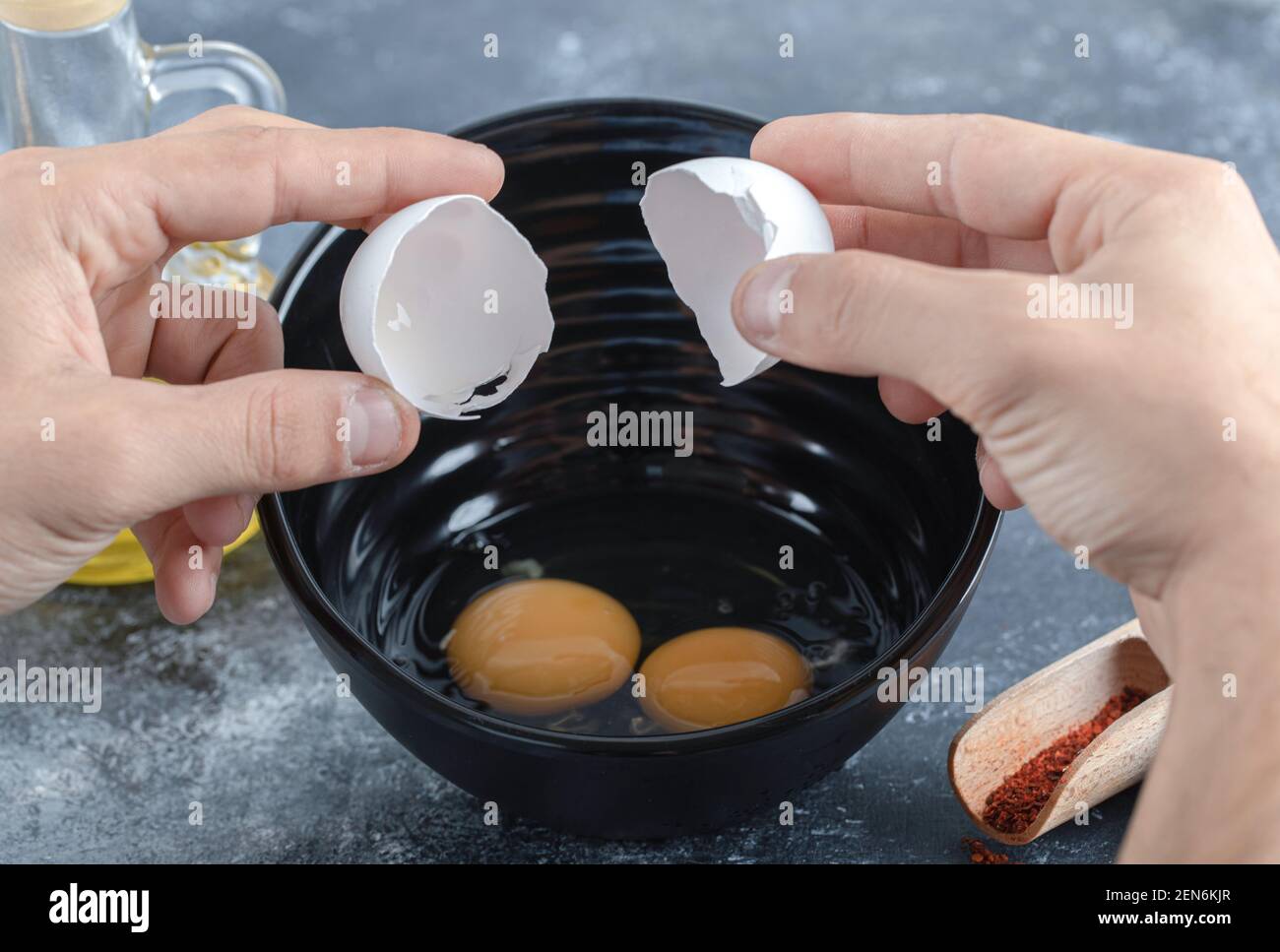Männliche Hände brechen Eier in schwarzer Schüssel auf grauem Hintergrund Stockfoto