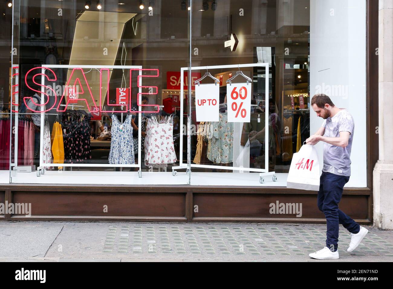 Ein Mann hält eine H&M-Einkaufstasche vor dem H&M-Kaufhaus in der Oxford  Street, wenn der Sommerverkauf beginnt. Viele Kaufhäuser bieten riesige  Rabatte, da sie Konkurrenz durch Online-Shopping gegenüberstehen. (Foto von  Dinendra Haria /