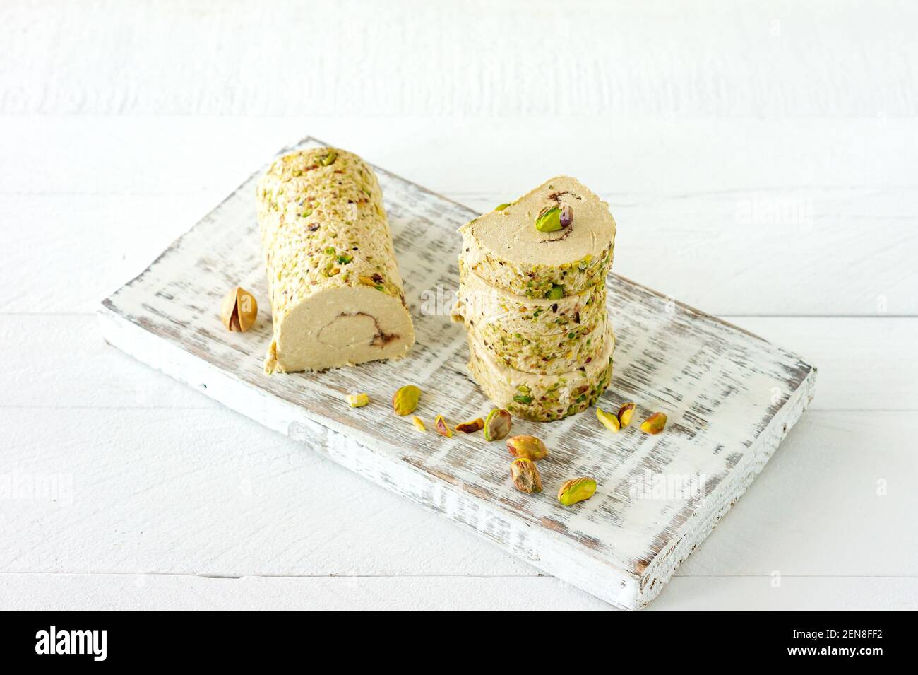 Halva mit Pistazie auf weißem Holzschreibtisch mit Blumen serviert. Stockfoto