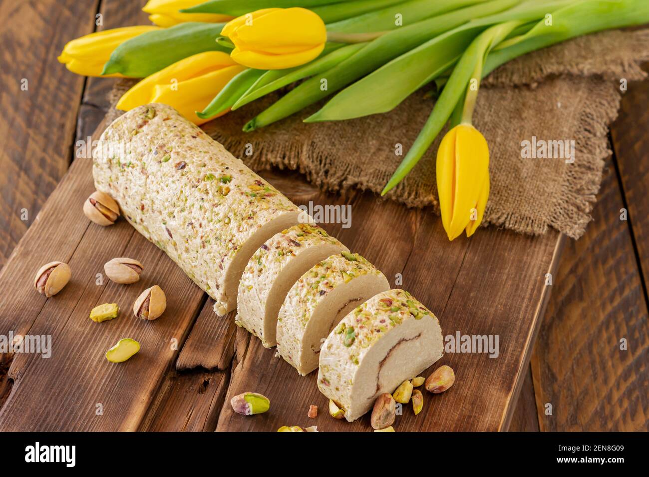 Tahini Halva in Scheiben mit Pistazie auf einem mit Blumen geschmückten Holzschreibtisch. Stockfoto