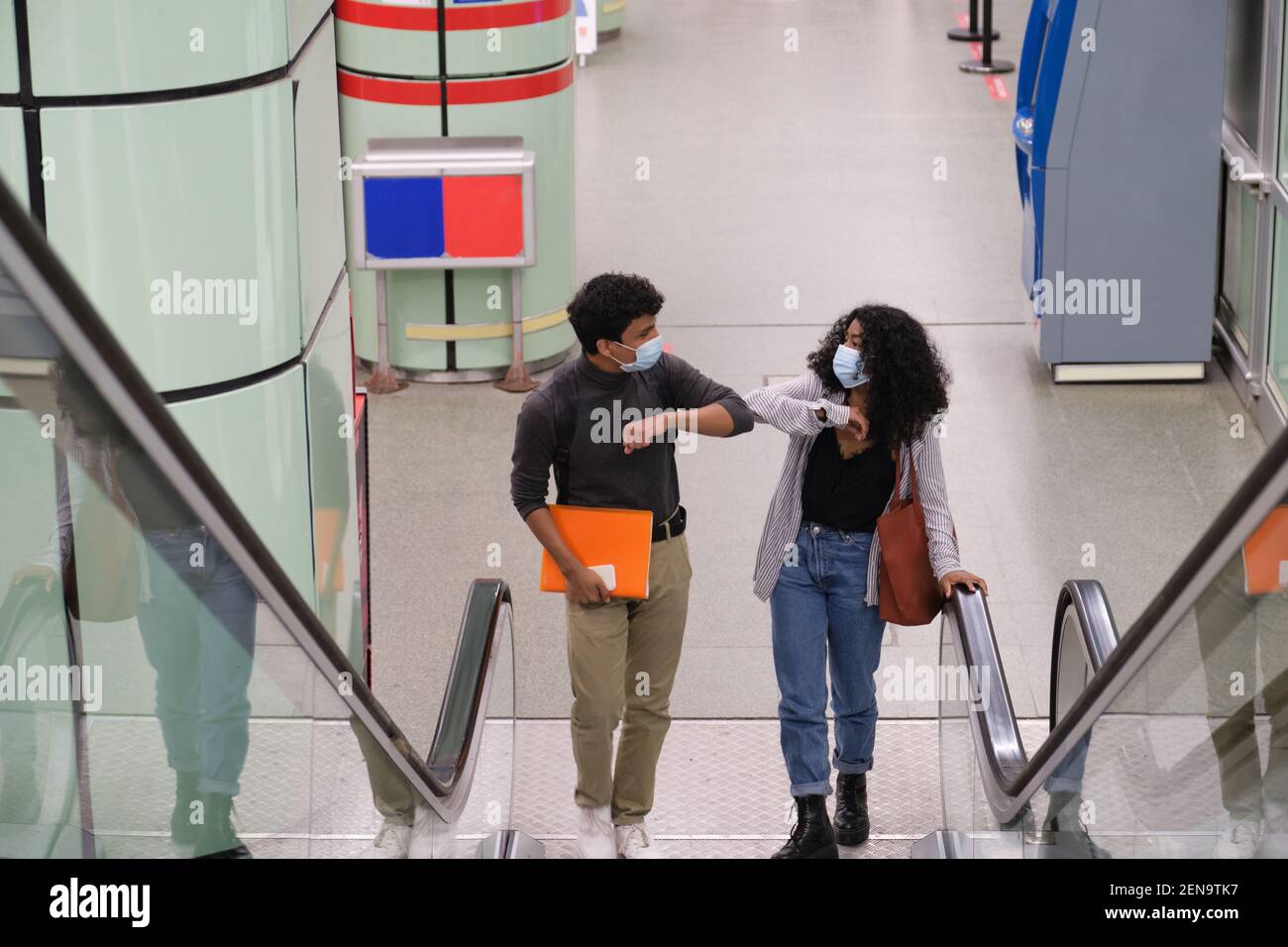 Junge lateinische Paar mit Schutzmaske tun Ellenbogen Beule Gruß an den Rolltreppen am Zug oder U-Bahn-Station. Neue Normalität bei öffentlicher Transportmittel Stockfoto