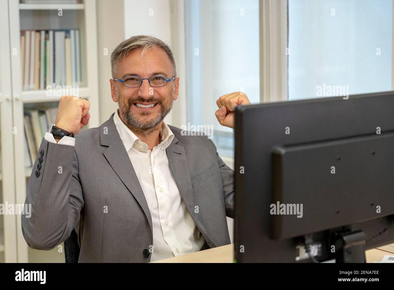 Erfolgreicher reifer Geschäftsmann sitzt am Office Desk, die Hand in Ja-Geste, feiert Geschäftserfolg. Lächelnd Aufgeregt Geschäftsmann Gesturing Stockfoto