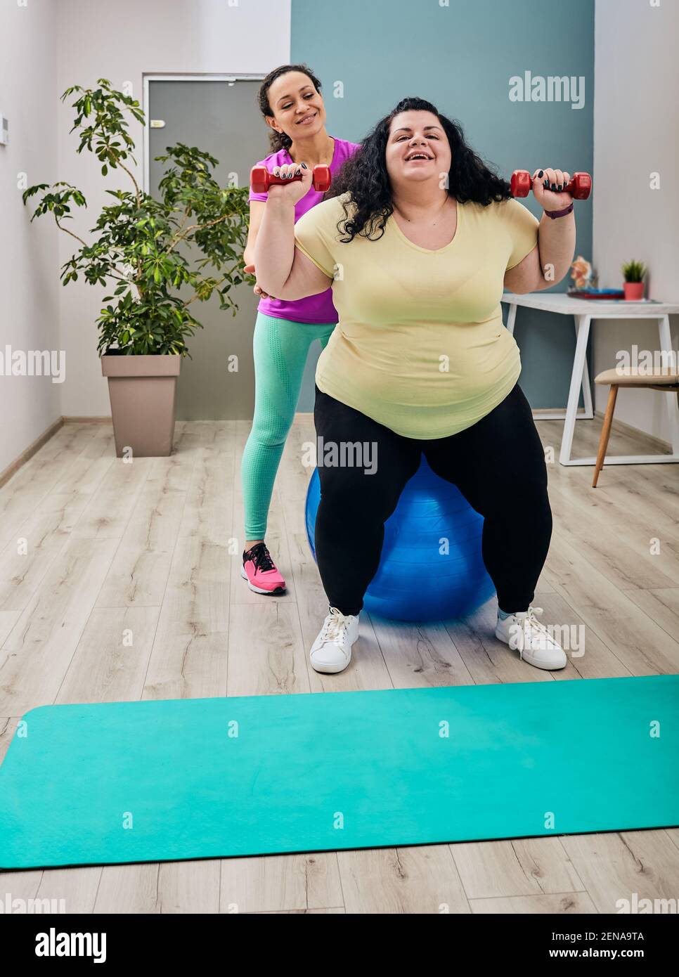 Übergewichtige Frau macht Übungen mit ihrem Trainer für die Gewichtsabnahme Mit Kurzhanteln und Fitness-Ball Stockfoto