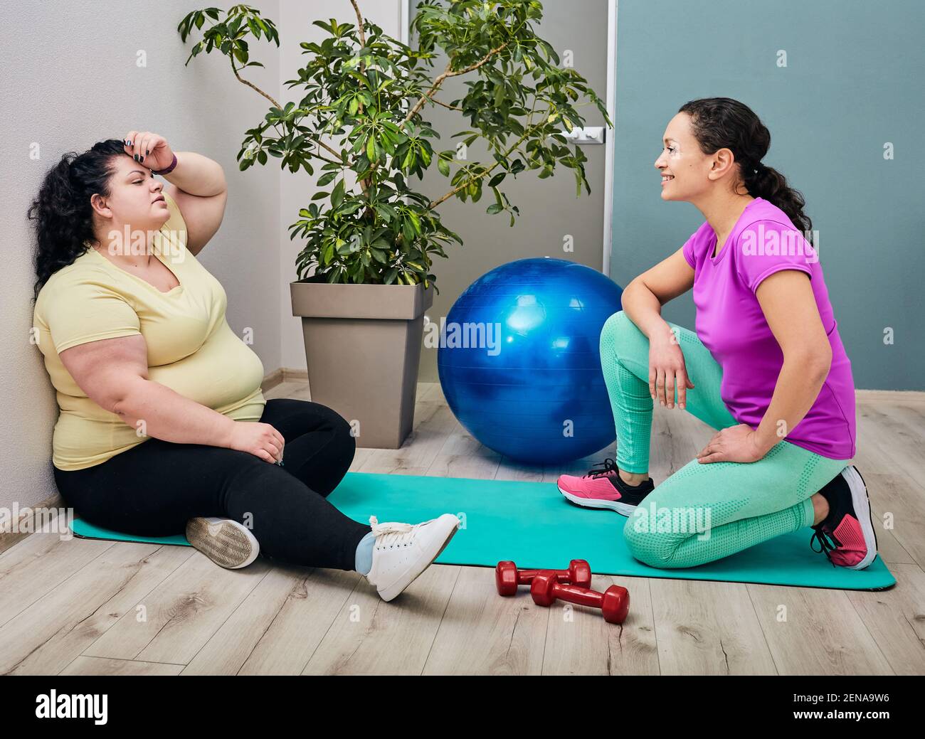 Müde übergewichtige Frau sitzt in der Turnhalle nach dem Training mit Ihr Trainer Stockfoto