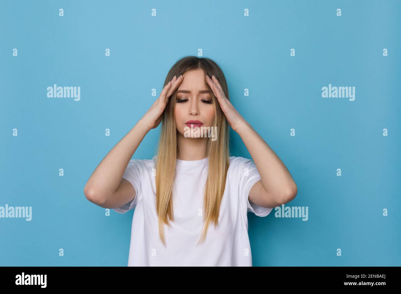 Junge Frau im weißen Hemd hat Kopfschmerzen und hält ihren Kopf in den Händen. Studio-Aufnahme auf blauem Hintergrund. Stockfoto