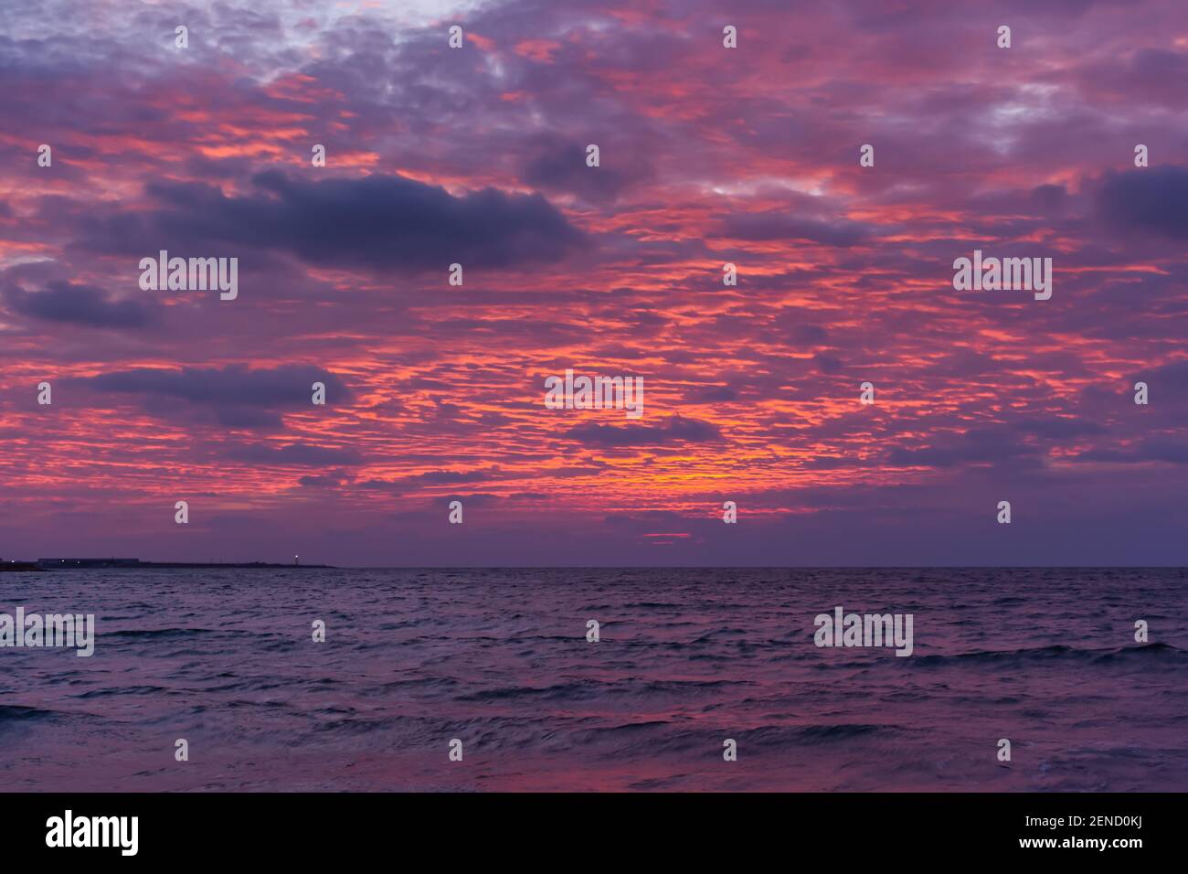 Rosa Sonnenuntergang auf dem Meer. Helle saftige Landschaft mit niedrigen Cumuluswolken am Horizont. Lila, lila und rosa Schattierungen des Abendhimmels. Wellen auf dem Stockfoto