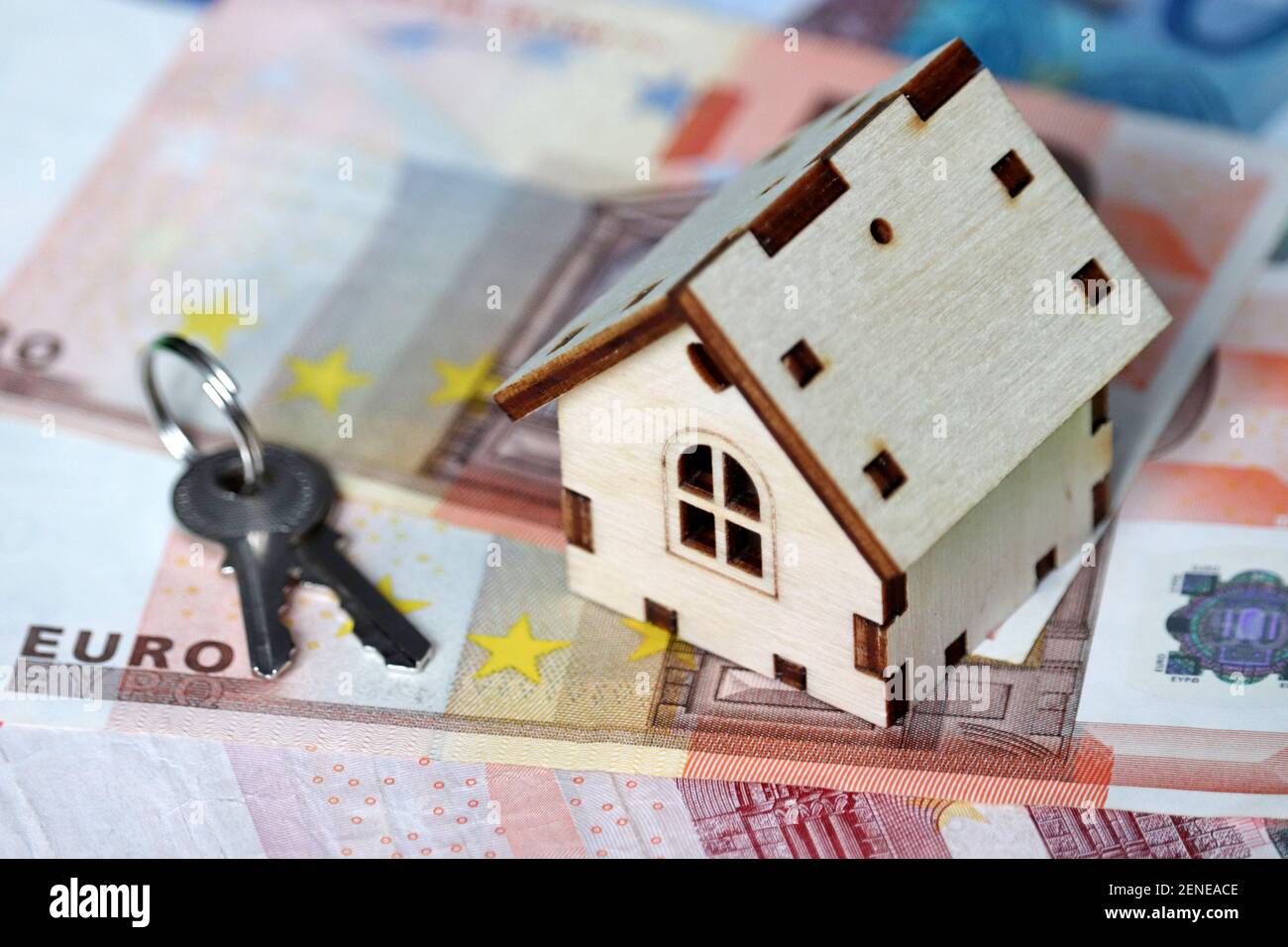 Holzhausmodell und Schlüssel auf dem Hintergrund der Euro-Banknoten. Wohnungsmarkt, Kauf oder Vermietung von Immobilien in Europa Stockfoto