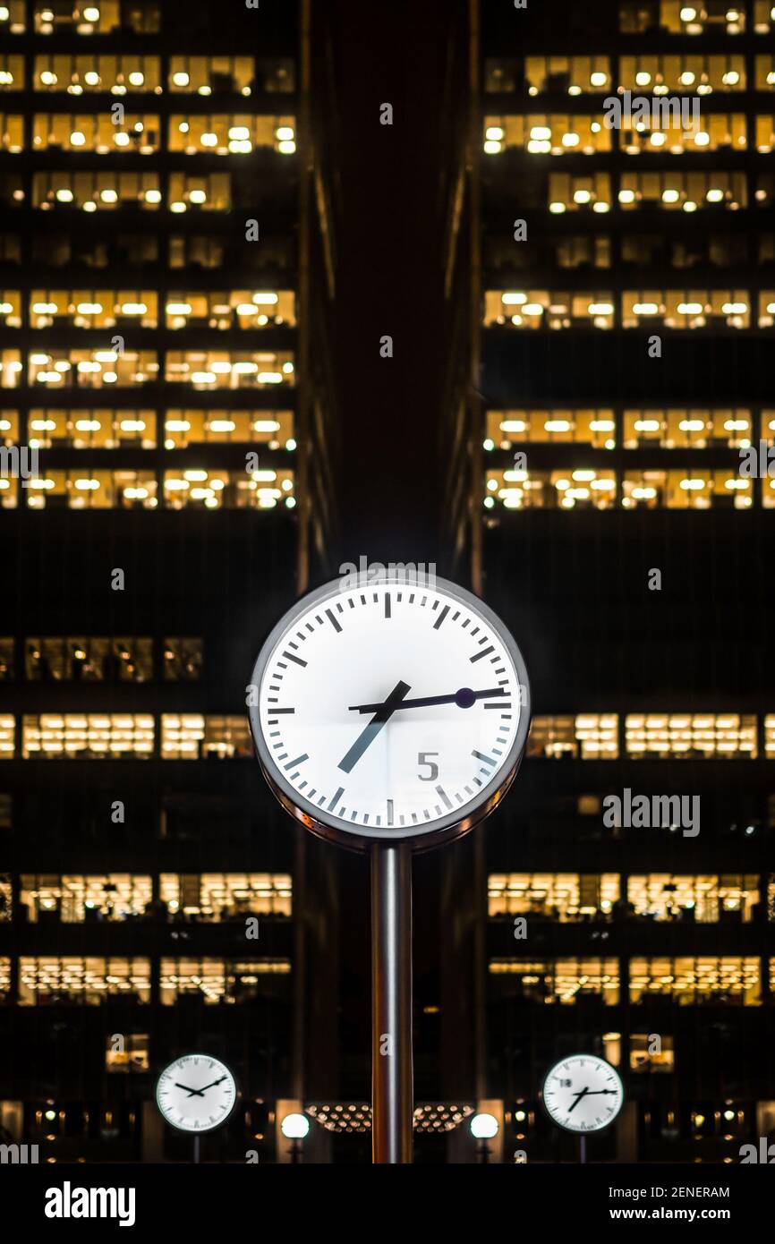 Canary Wharf, London Oktober 29th 2020 große Edelstahluhren zeigen die Zeit mit Wolkenkratzern, die hinter den nächtlichen Fenstern stehen, die im Dunkeln beleuchtet sind Stockfoto