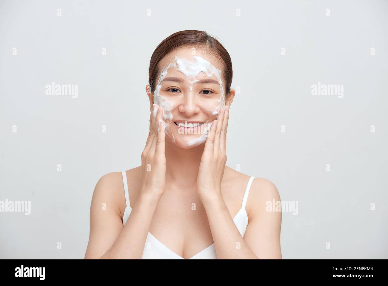 Fröhliche asiatische Frau Anwendung schäumende Reinigungsmittel, hat saubere frische gesunde Haut. Stockfoto