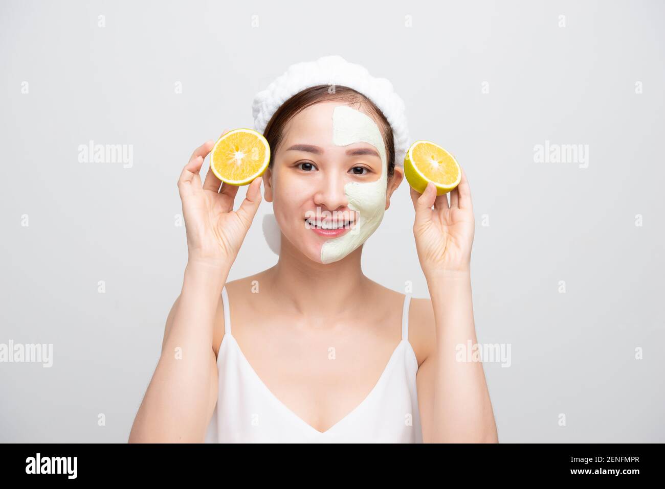 Hübsche asiatische junge Frau Maske feuchtigkeitsspendende und verjüngende saubere Haut Peeling, während halten orange Stücke über weißem Hintergrund. Stockfoto