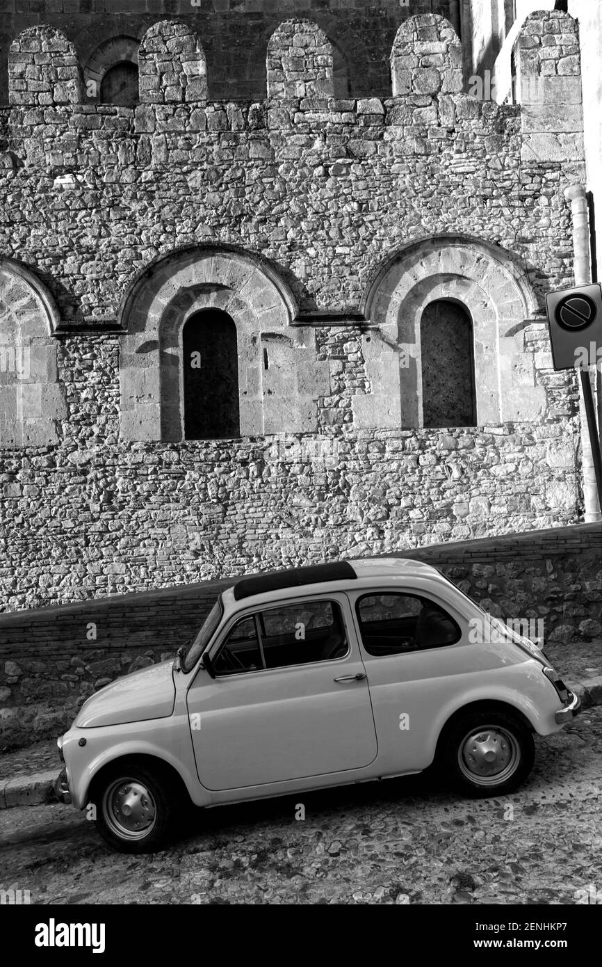 Italien, Sizilien, Cefalu, antikes Fiat Cincocento 500 Auto, das auf einer gepflasterten Straße gegen eine mittelalterliche Struktur geparkt ist Stockfoto