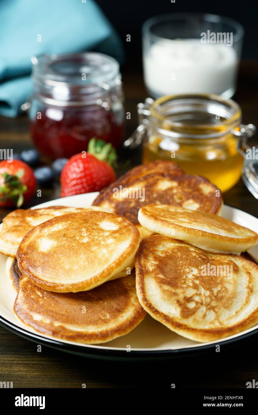 Blini serviert mit Erdbeermarmelade, Honig, Sauerrahm und frischen Beeren. Dunkler Holztisch, hohe Auflösung Stockfoto