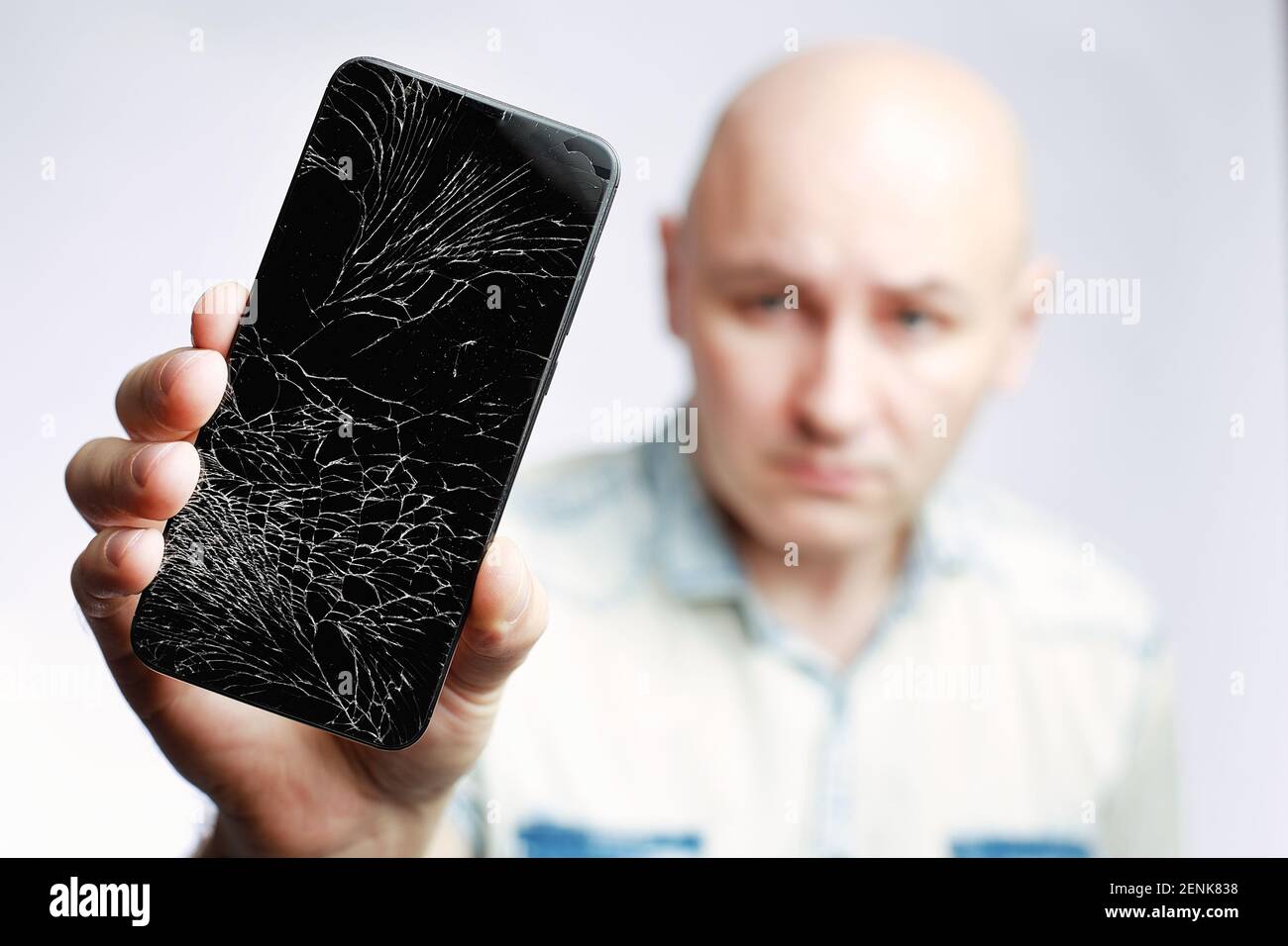 Telefon mit EINEM defekten Bildschirm Nahaufnahme. Ein weißer Mann hält ein schwarzes Smartphone mit einem geknackten Display. Stockfoto