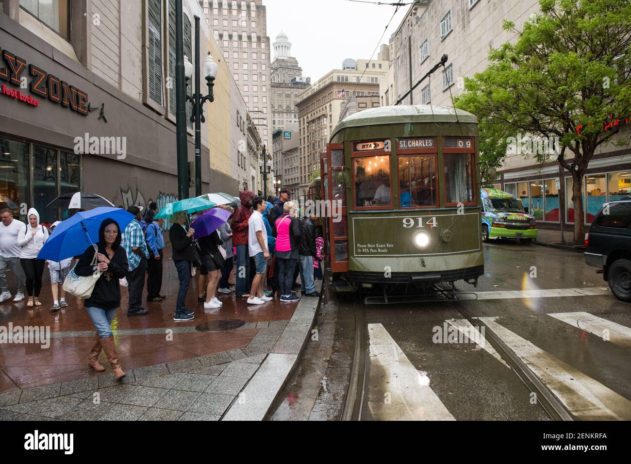 Passagiere drängen sich unter farbenfrohen Regenschirmen, während sie an einem regnerischen Tag auf der belebten Canal Street an Bord der legendären New Orleans Straßenbahn gehen. Stockfoto