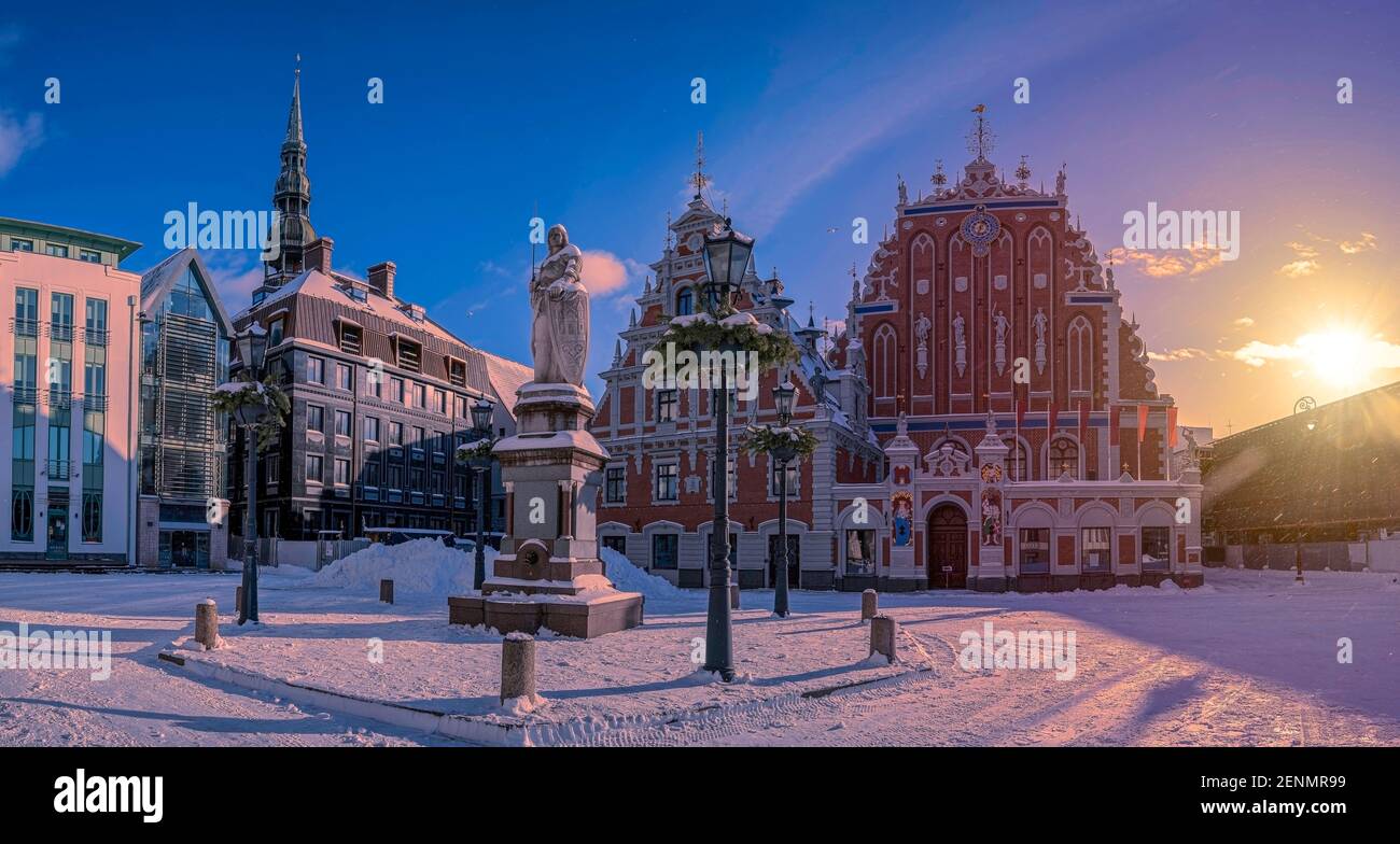 Sonnenuntergang über Schnee Rathausplatz Riga im Winter in Riga, Lettland. Blick auf das berühmte Haus der Schwarzköpfe und Rolands Statue Stockfoto