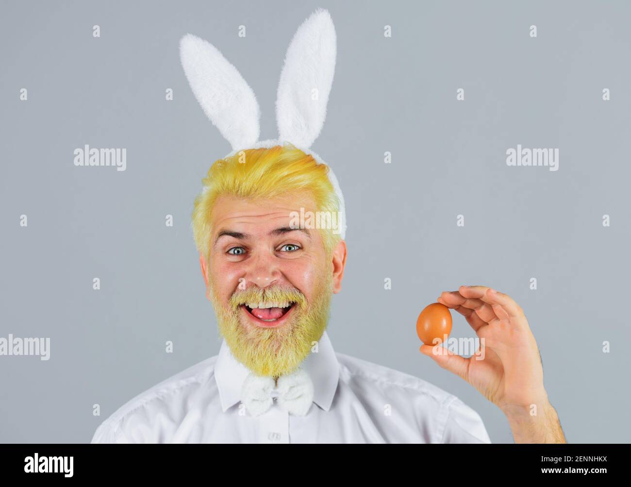 Glücklicher Mann mit Kaninchenohren mit Osterei. Männchen in Hasenohren. Eiersuche. Frühlingsferien. Stockfoto