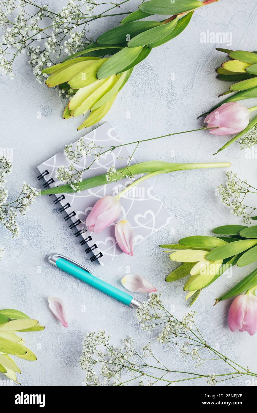 Arbeitsbereich mit Tagebuch, Notizbuch, Stift, Blumen auf hellblauem Hintergrund. Schreibtisch im Home Office. Draufsicht femininer Hintergrund. Flach liegend, Draufsicht. Stockfoto