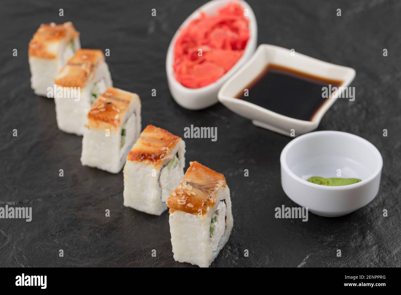 Sushi-Rollen, Wasabi, Soja und eingelegter Ingwer auf schwarzer Oberfläche Stockfoto