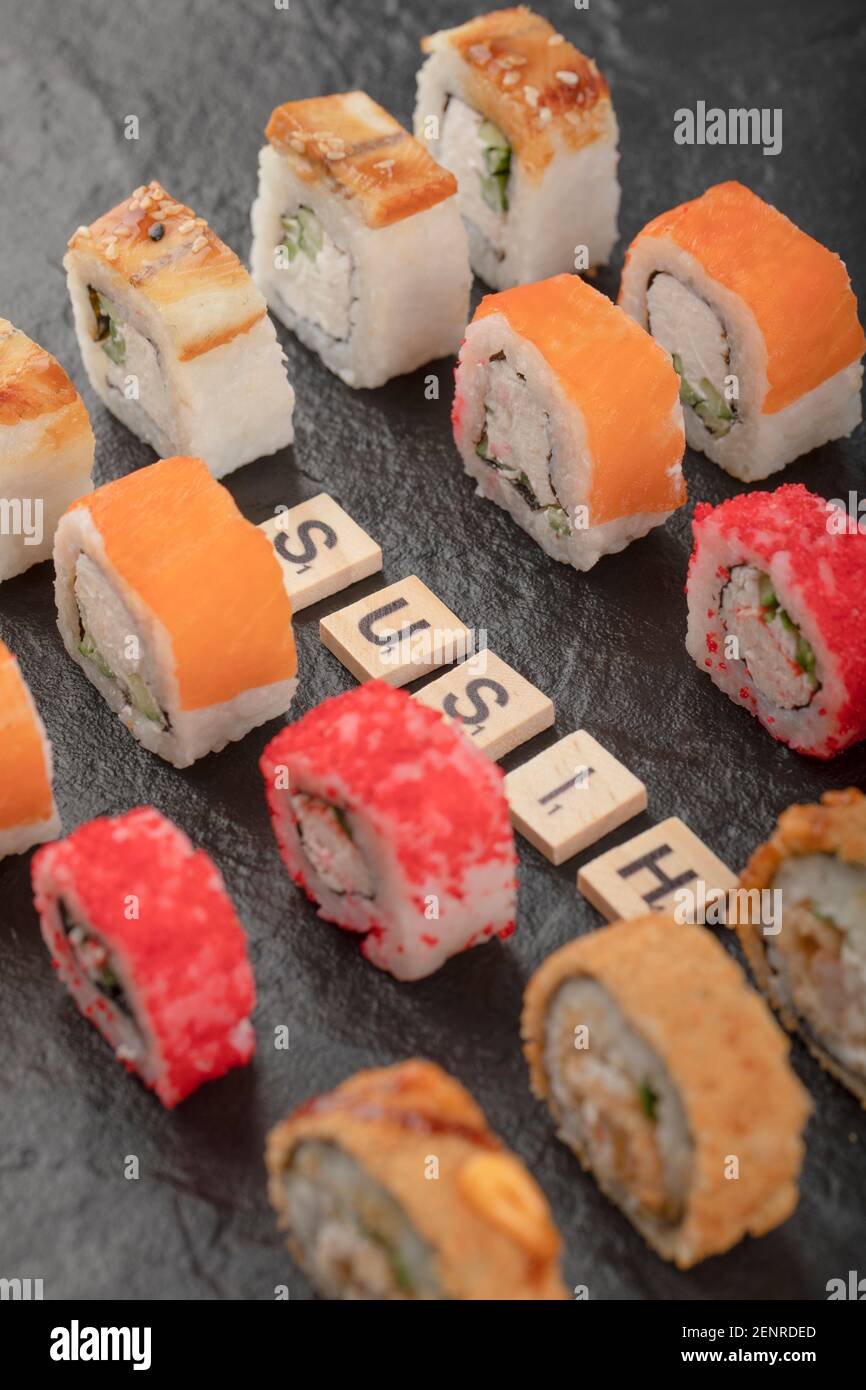 Set von Sushi-Rollen mit Holzbuchstaben geschrieben als Sushi Auf schwarzer Oberfläche Stockfoto