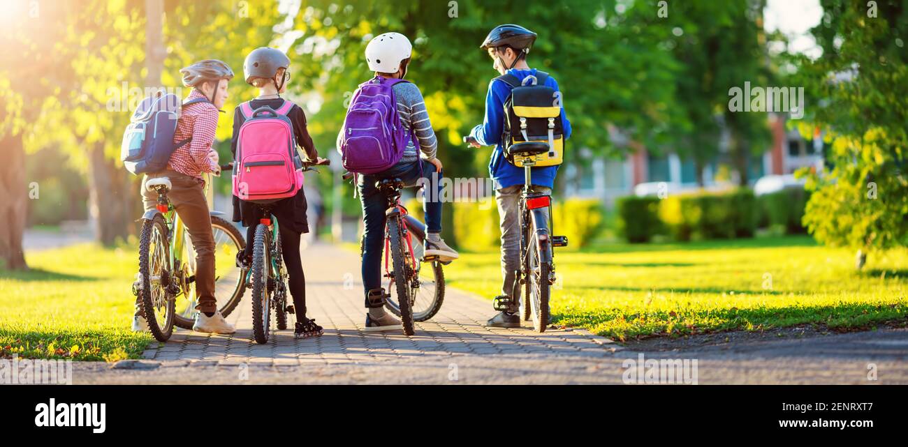 Kinder mit Rucksäcken reiten auf dem Fahrrad im Park in der Nähe der Schule Stockfoto