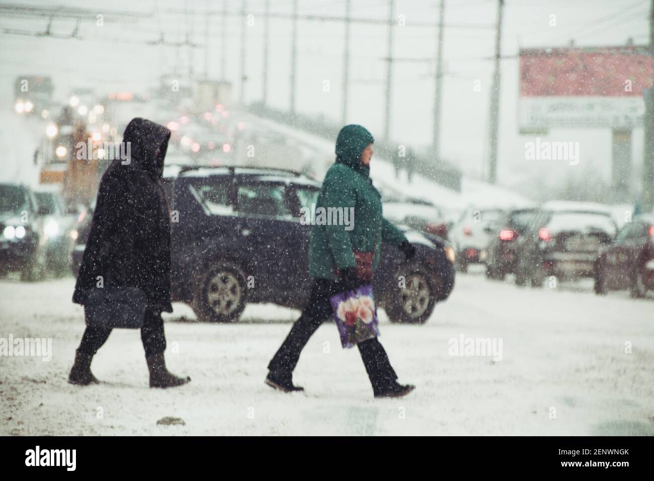 Menschen überqueren die Straße bei stürmischem Schneewetter in seichtem Schärfentiefe mit Autos im Hintergrund Stockfoto