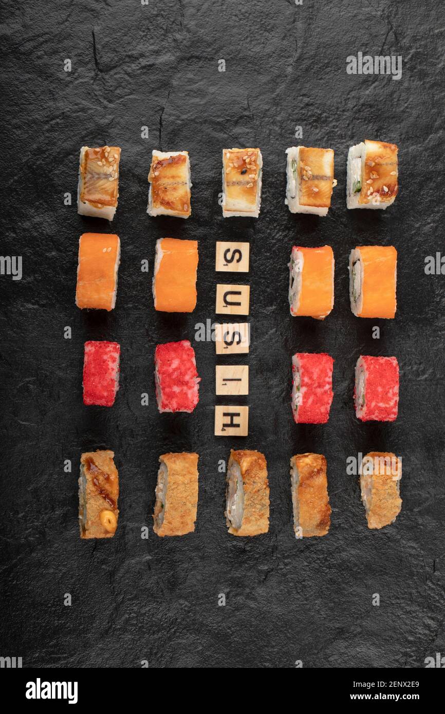 Set von Sushi-Rollen mit Holzbuchstaben geschrieben als Sushi Auf schwarzer Oberfläche Stockfoto